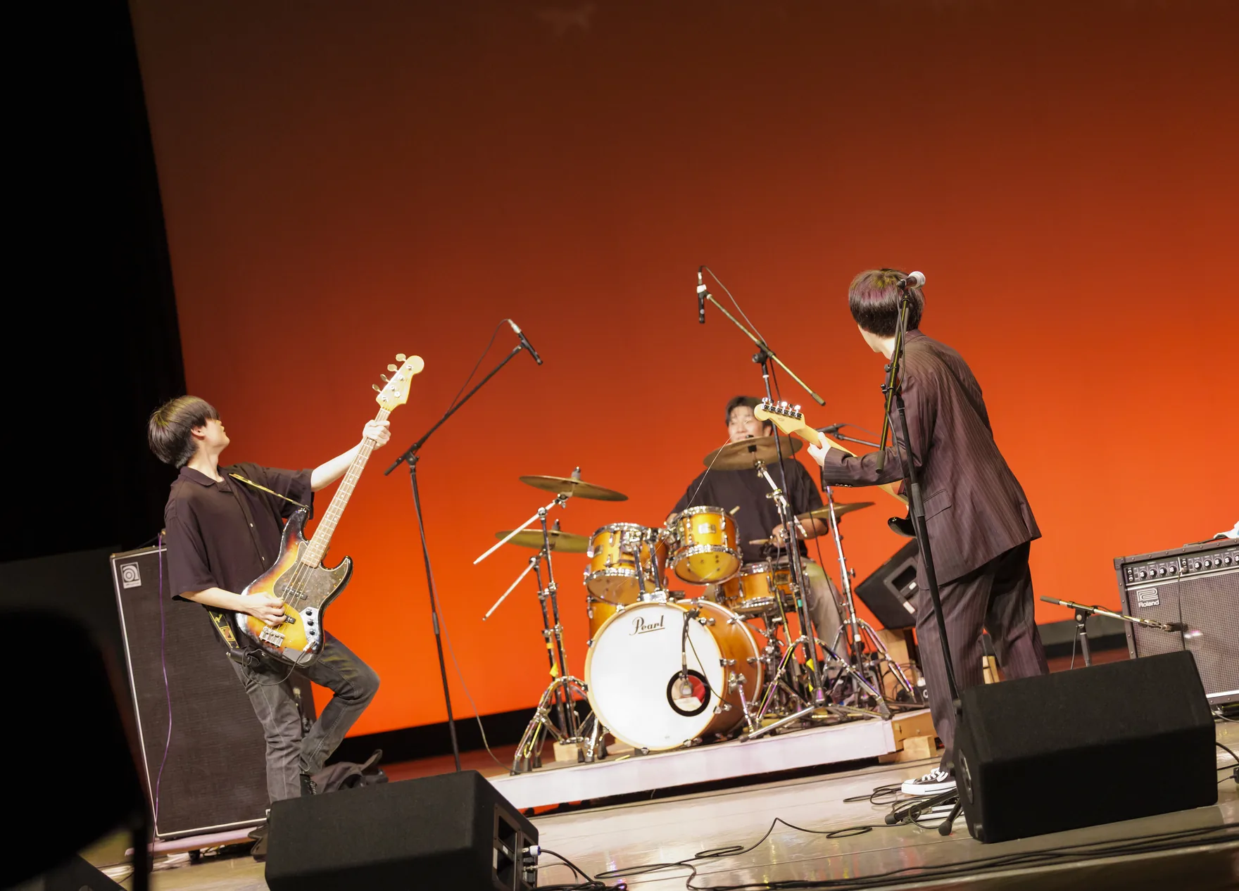 ホールのステージでギターとドラムを演奏するバンドの出演者たち
