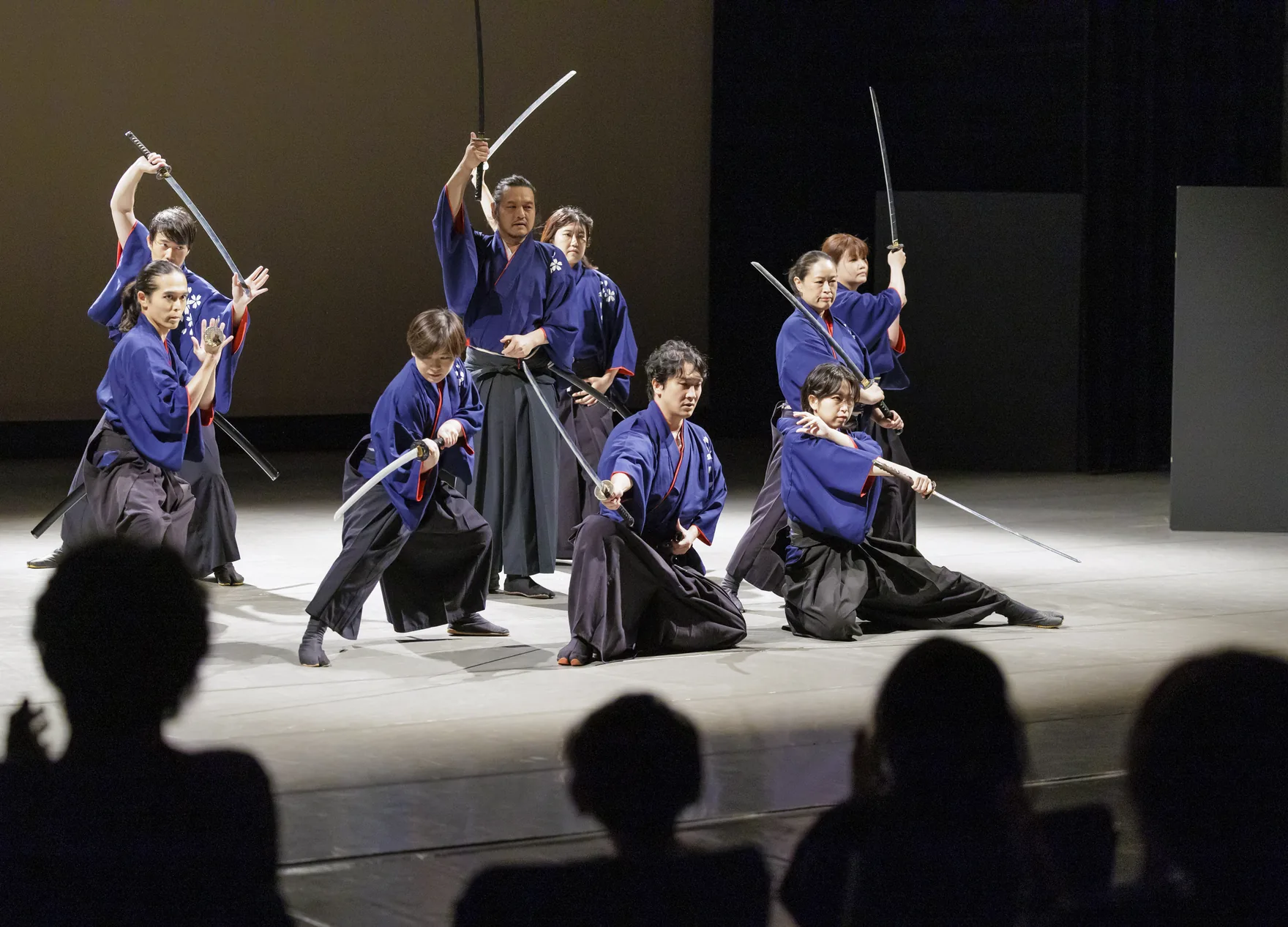 藍色の衣装で刀を構え、ホールのステージで演じる剣舞の出演者たち